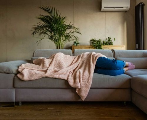 Woman with hangover lying on couch with blanket over her head