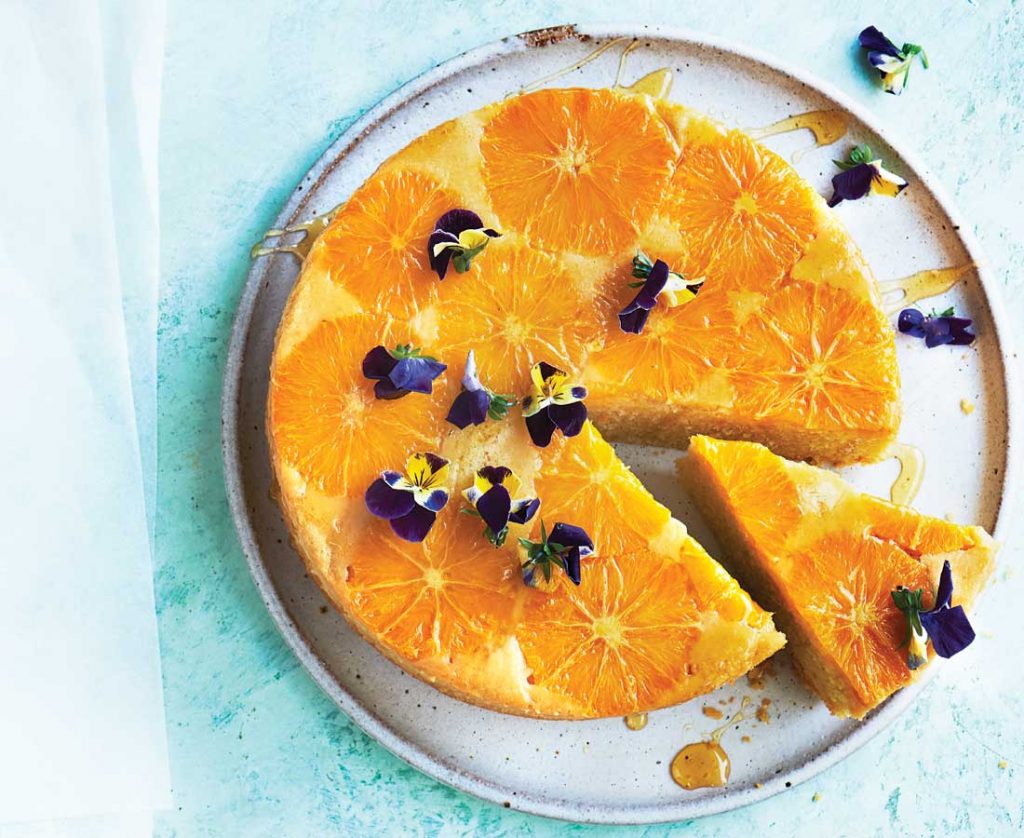 Upside-down orange and almond cake with rosewater yoghurt Orange and almond cake on a light blue background with a piece slightly out of it