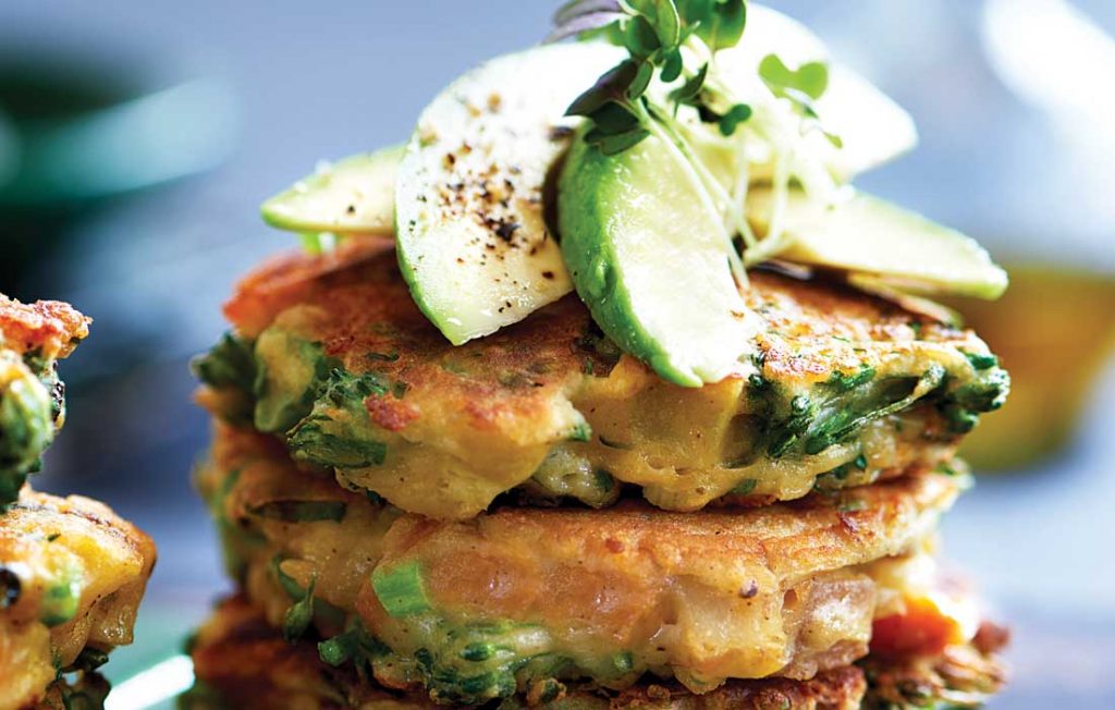 Vege fritters with sweet chilli and sour cream a pile of vegetable fritters topped with avocado